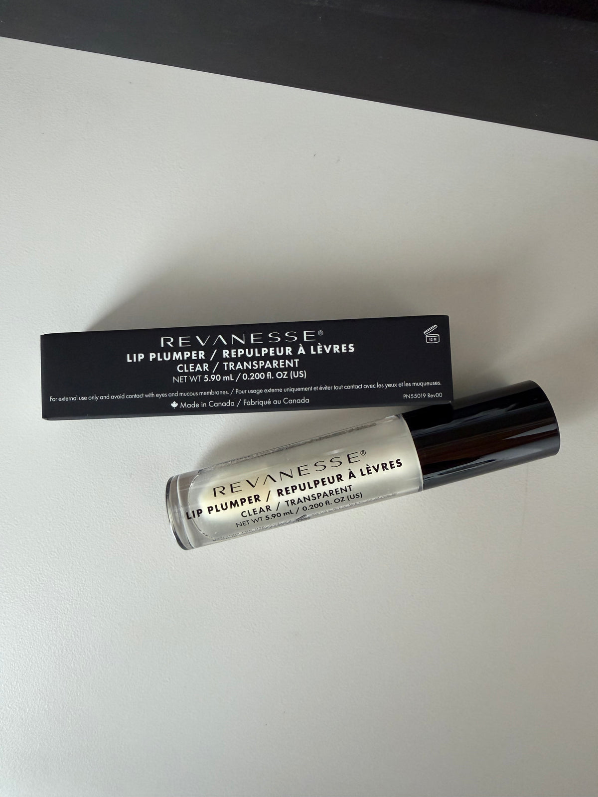 Revanesse Clear Lip Plumper's silver and black tube beside its black box on a white surface, at LADA Beauty, Las Cruces
