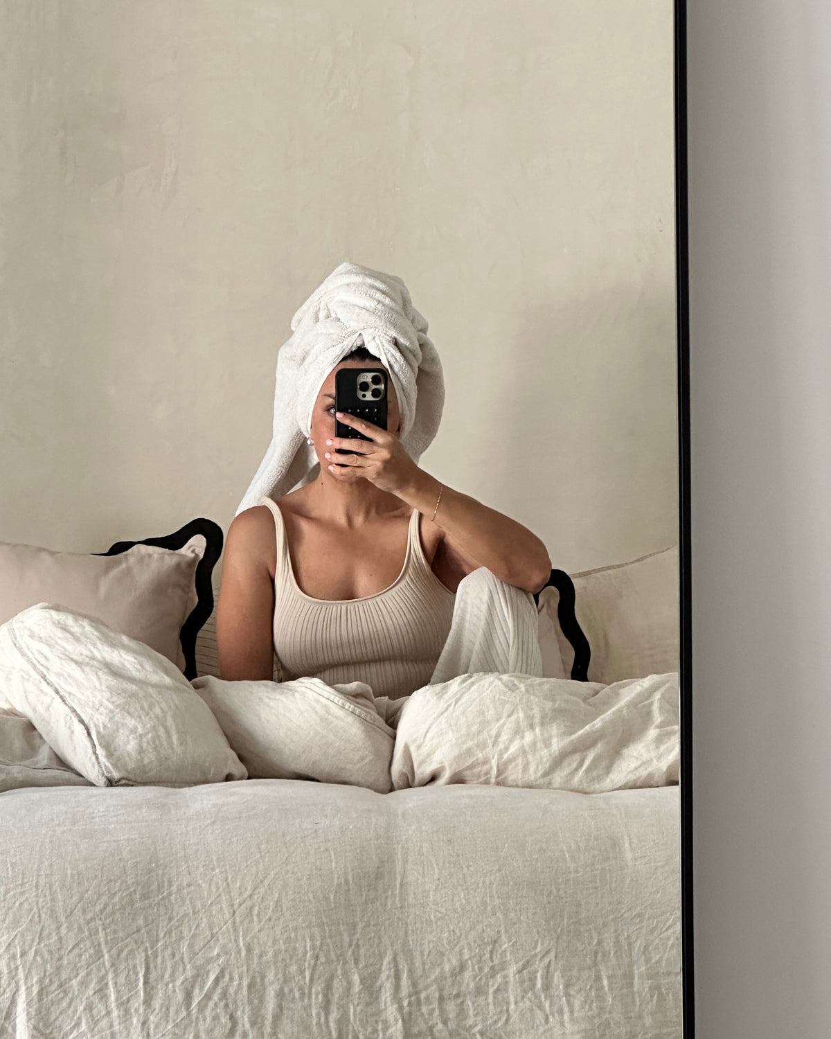 Person wrapped in a towel sitting on a bed in a neutral-colored room, relaxing during an at-home skincare routine with LADA Beauty, serving El Paso, TX